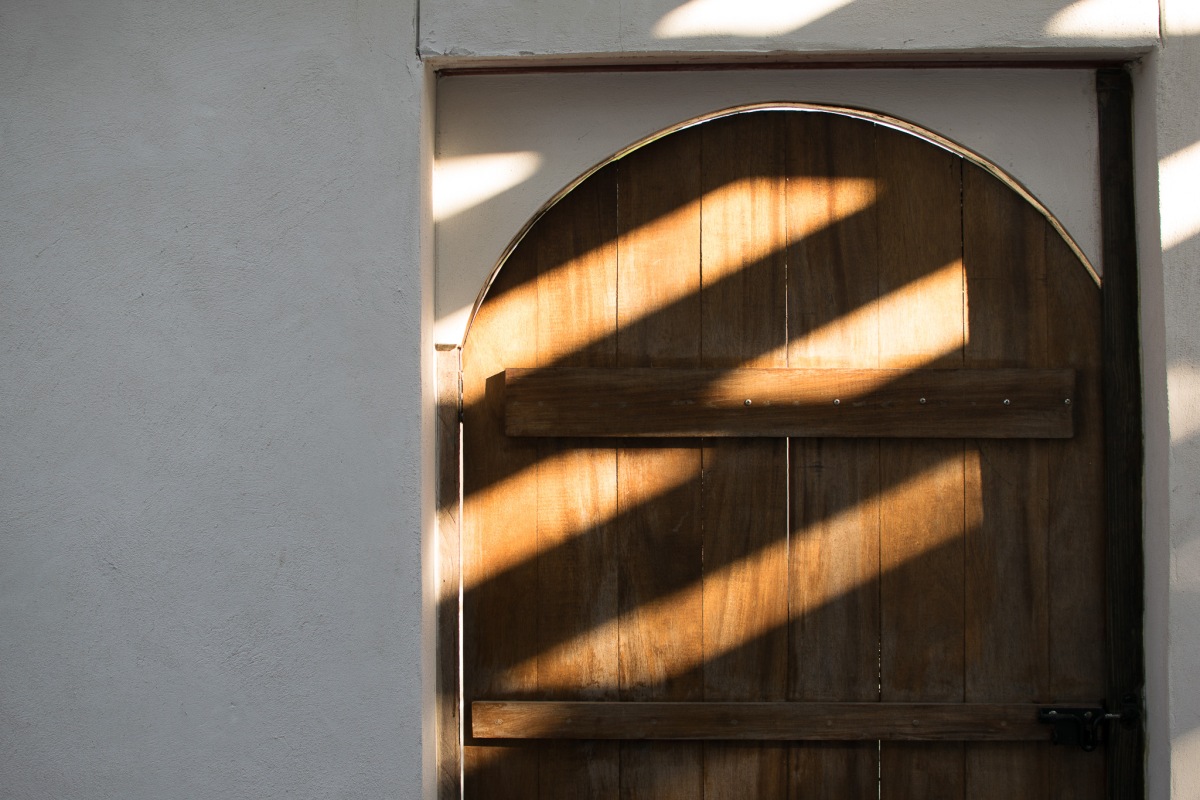 A partial photo of a wooden arched door and the stucco wall beside it.